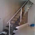 Escalera metálica con eje de tubo estructural y peldaños de palastro y barandilla en acero inoxidable y cristal laminado