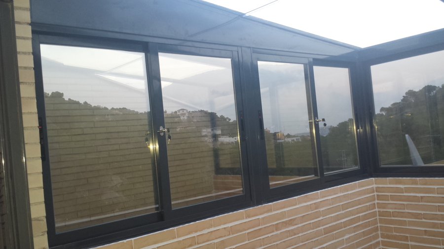 Cerramiento total terraza ladrillo visto ventanas y techo aluminio y cristal.