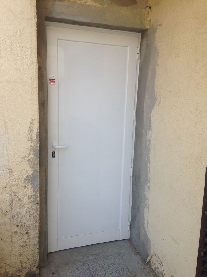 Puerta E.E.B. Primera de Sabadell de aluminio blanco serire Alba ciega, con cerradura y freno.