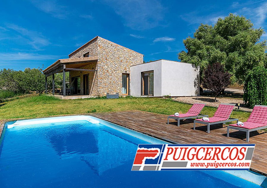 Piscina de fibra y fachada con porche de piedra viva sin junta y hormigón blanco.