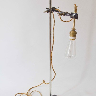 Original lámpara vintage realizada con tripode de los años `50. El casquillo es cerámico e incluye una bombilla incandescente. Cuenta con un regulador para el encendido y apagado. Lleva enchufe.
