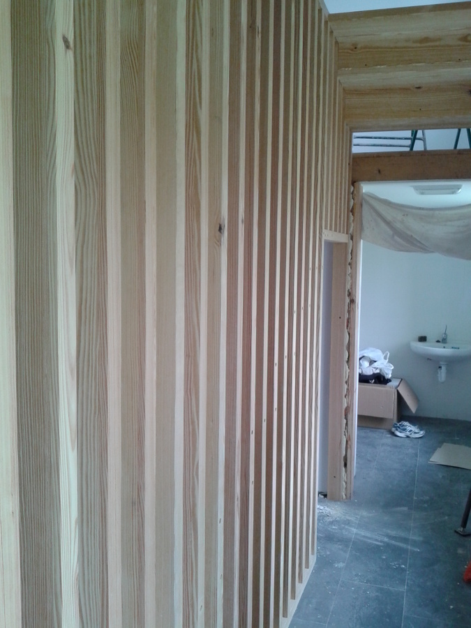 Celosía estructural de madera, tamizando la vista del acceso a los aseos