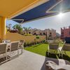 Terraza de casa adosada con zona de comedor, jardín y toldo con brazos.
